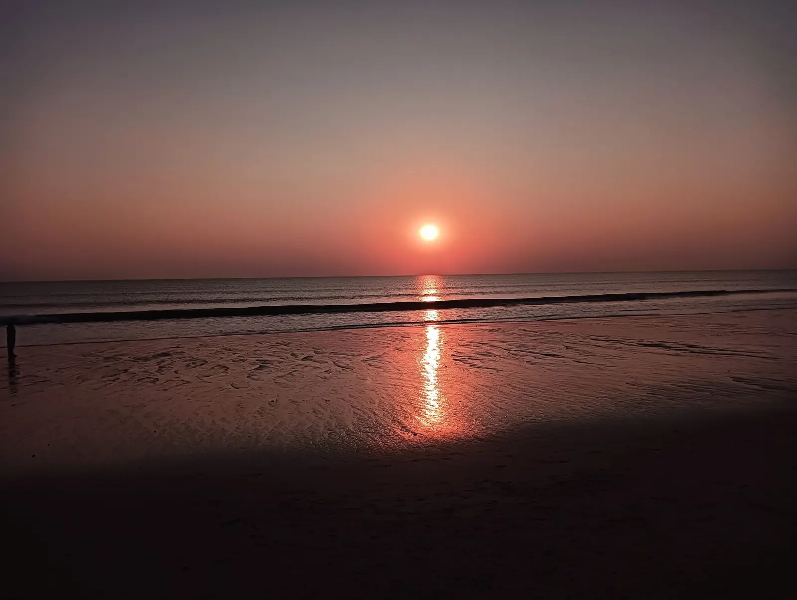 Sun setting over a calm beach, reflected in the wet sand