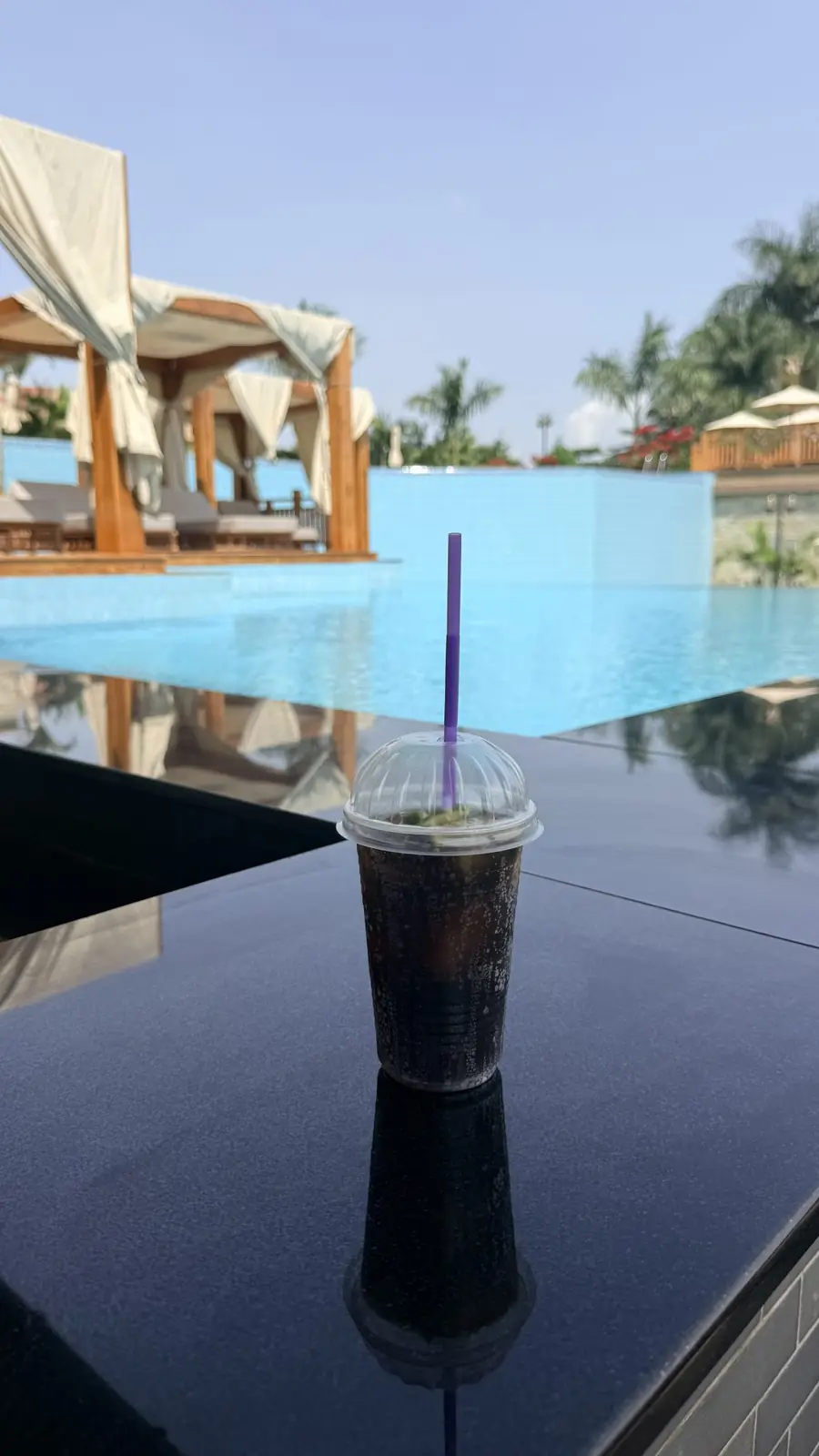 Iced drink on a poolside table with cabanas behind