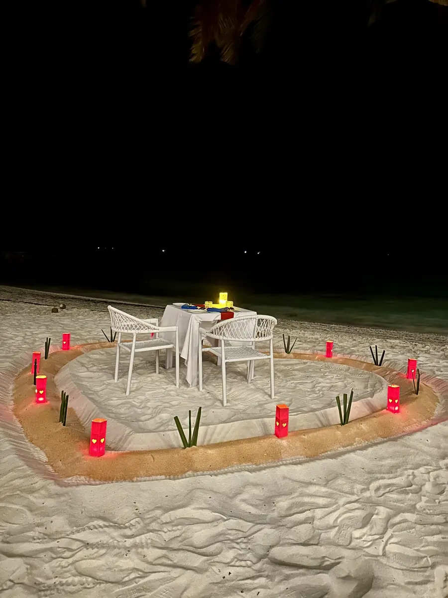 Candlelit private dinner table set on the sand at night