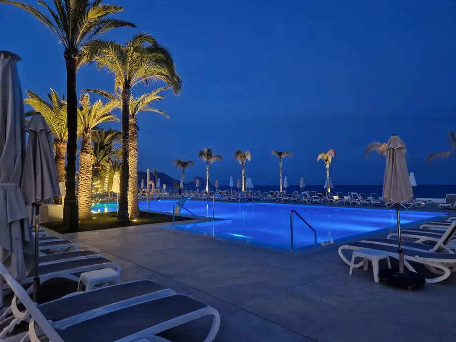 Resort pool lit blue at night under palm trees